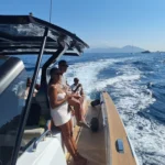 A group of tourists enjoying a boat trip along the Amalfi Coast, with waves splashing behind the boat