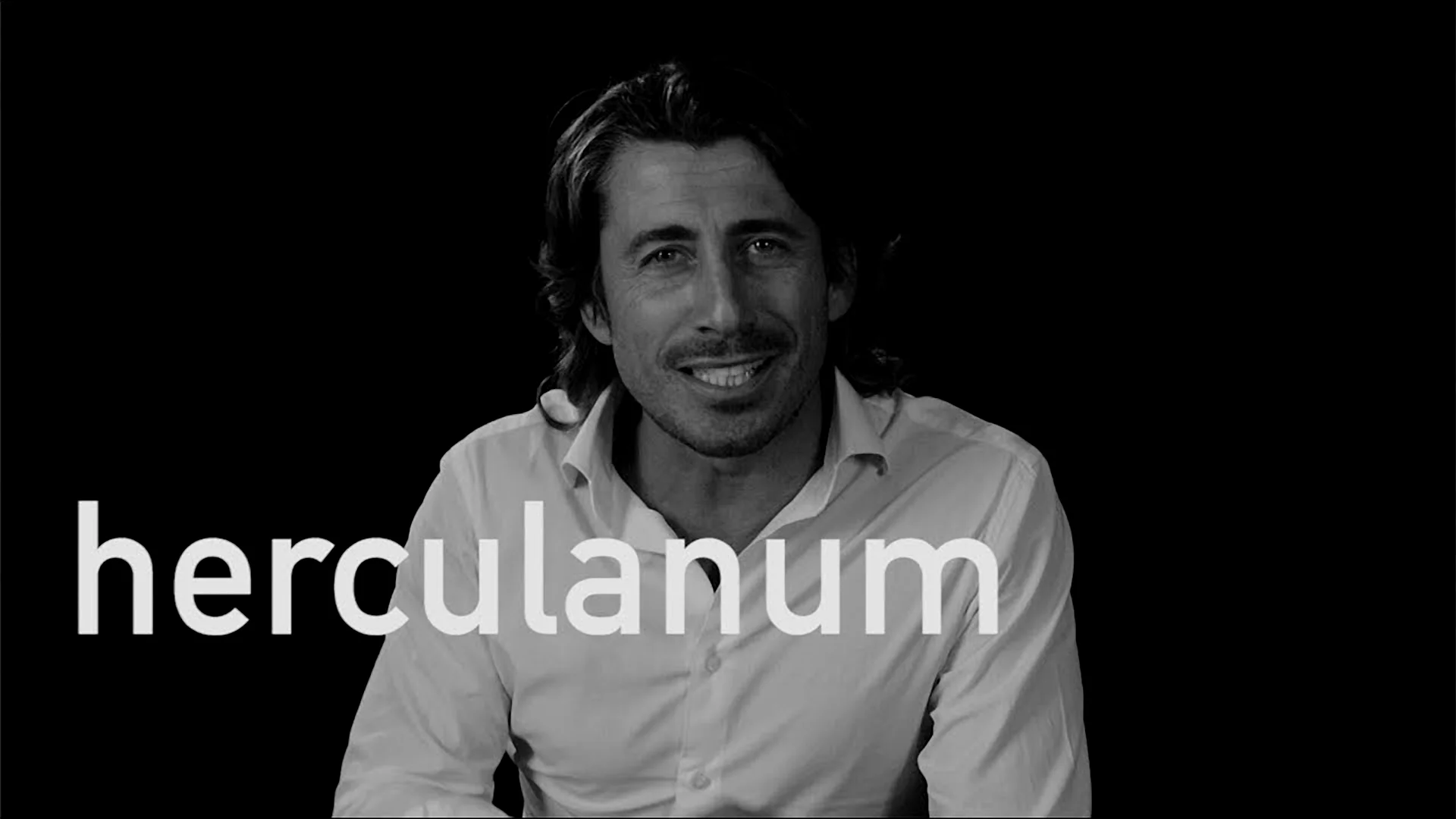 Luca in white shirt on dark background explaining Herculaneum archaeological site.